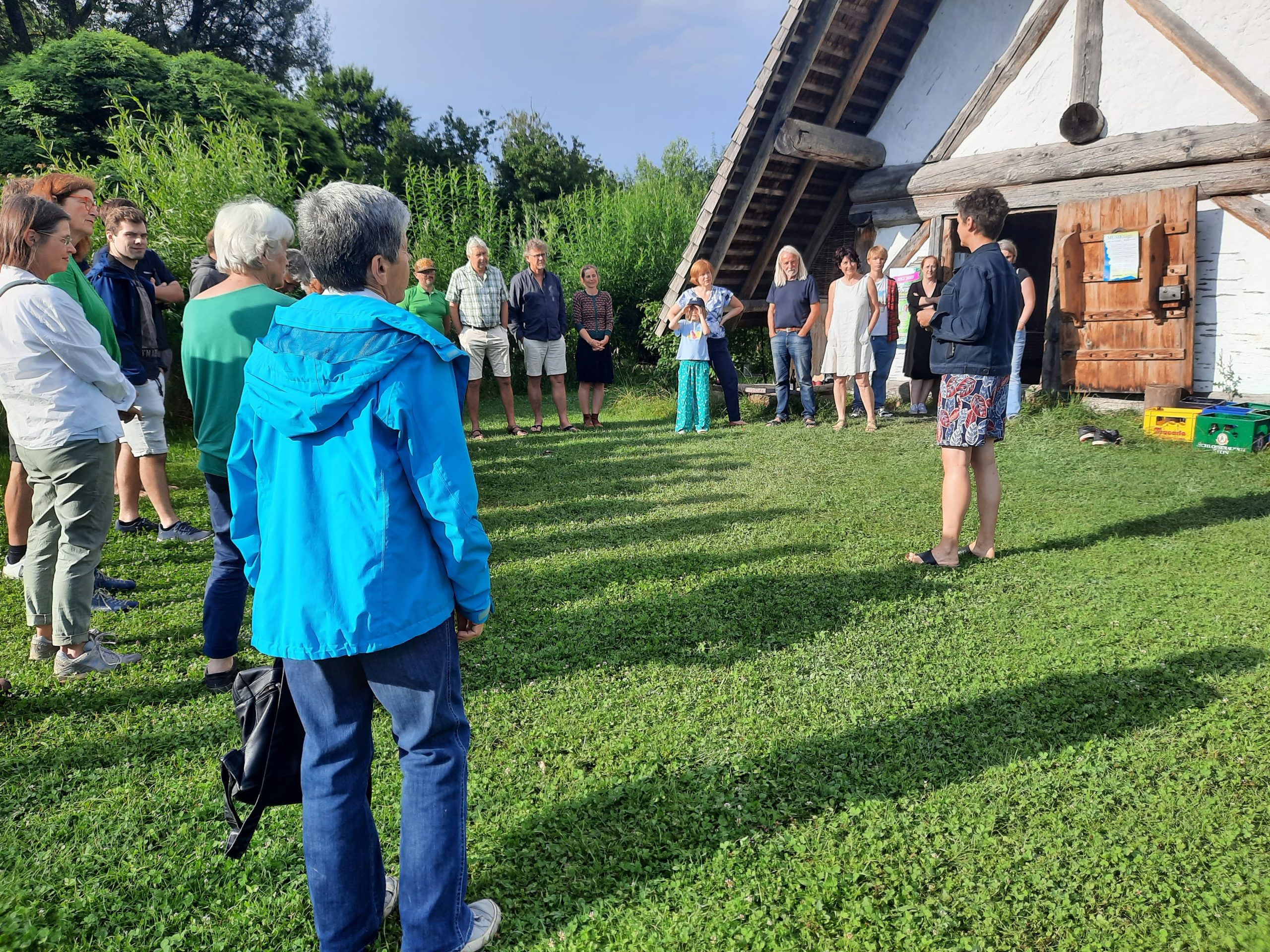 Vor dem historischen Haus der Bajuvaren steht eine Gruppe Menschen im Halbkreis und hören einer Rednerin zu.