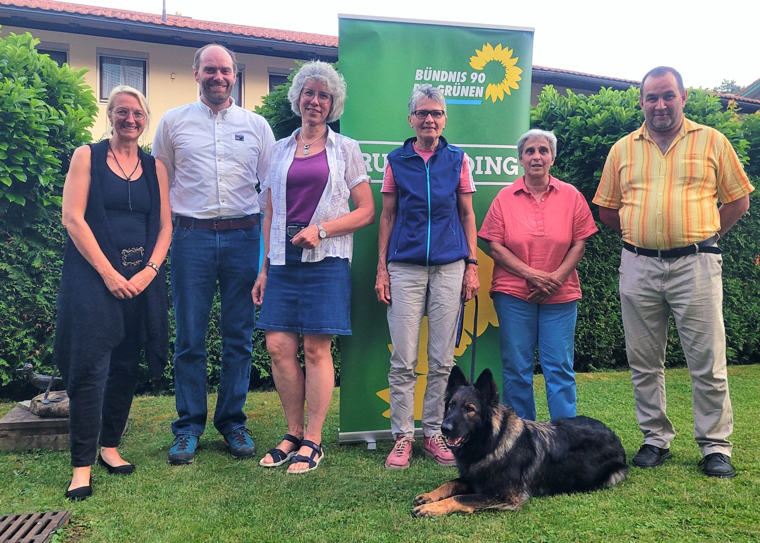 In einem Garten vor dem Banner der Grünen OV Ruhpolding steht der neugewählte Vorstand. Im Vordergrund liegt ein Hund.